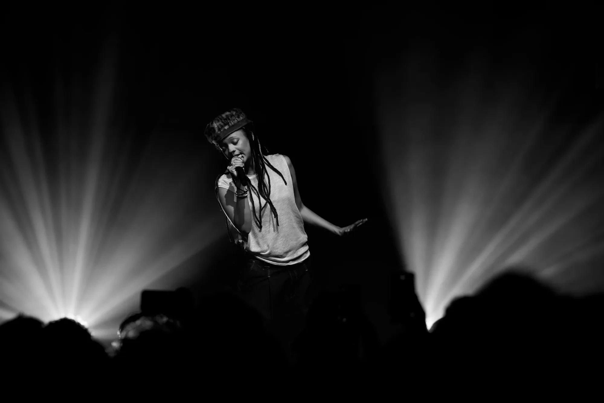 Chanteuse en noir et blanc sur scène, rayons lumineux et public en silhouette